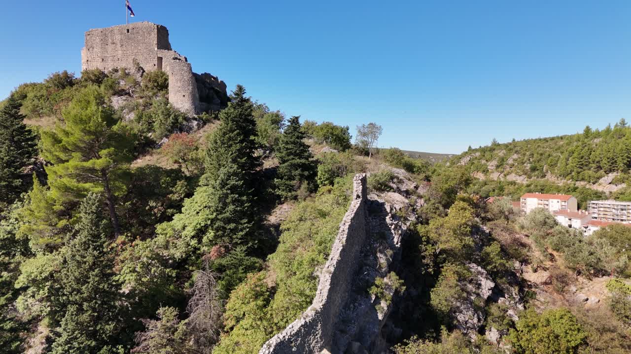 Drone lift-off revealing Kurjaković Fortress above Obrovac and the green Zrmanja River flowing below — history and nature meet in Dalmatia