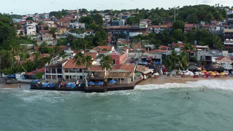 Dolly-out-rotating-aerial-drone-shot-of-the-beautiful-pink-Saint-Sebastian-Chapel-in-the-famous-tropical-tourist-beach-town-of-Pipa,-Brazil-in-Rio-Grande-do-Norte-on-a-warm-sunny-summer-evening