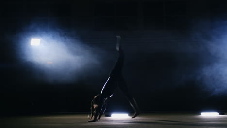 talented girl gymnast performs flips on the gymnastics carpet in slow motion in the light in the smoke.