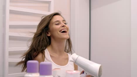 Cheerful-woman-drying-her-hair-in-bathroom