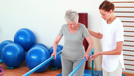 physical therapist helping patient walk with parallel bars