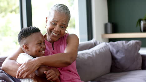 Glücklicher-Afroamerikanischer-Enkel-Und-Großmutter-Kuscheln-Auf-Dem-Sofa,-Kopierraum,-Zeitlupe