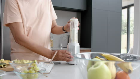 Midsection-of-senior-biracial-man-blending-healthy-smoothie-in-kitchen,-copy-space,-slow-motion