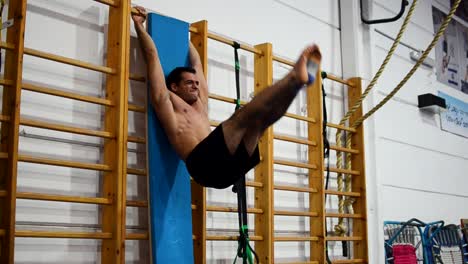 a guy in a gymnastics gym doing leg raises on a ladder and uneven bars still shot diagonal view