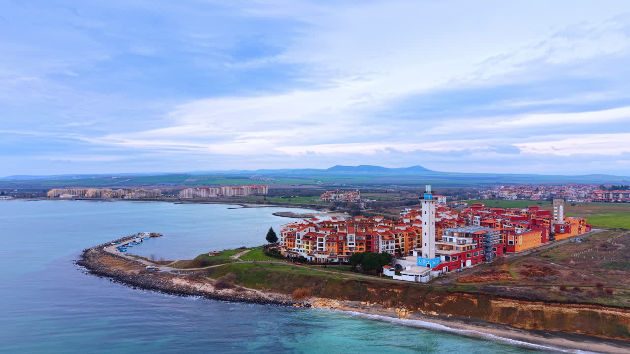 Panoramisk kystudsigt over et fyrtårn og kystbyarkitektur. Bredt luftperspektiv af et fyrtårn og rødtagede bygninger beliggende på en halvø ved havet.