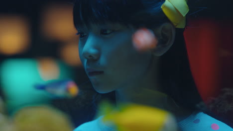 asian girl looking at fish in aquarium curious child watching colorful sea life swimming in tank learning about marine animals in underwater ecosystem inquisitive kid at oceanarium