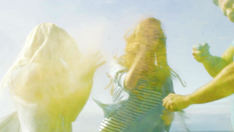 multi-ethnic group of young people throw colorful powder at each other in celebration of holi festival. they have enormous fun on this clear day by the sea.