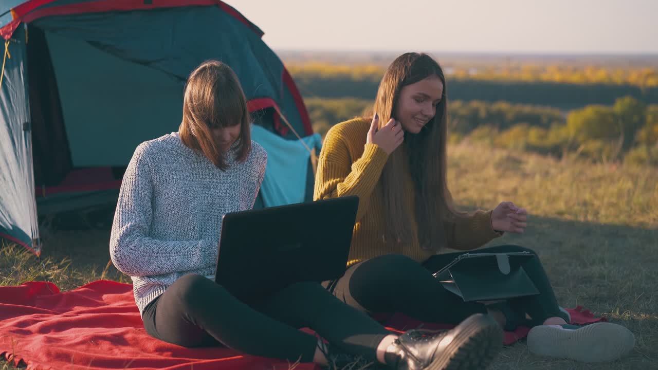 las niñas usan tableta y computadora portátil sentadas en una tienda de campaña en la orilla del río