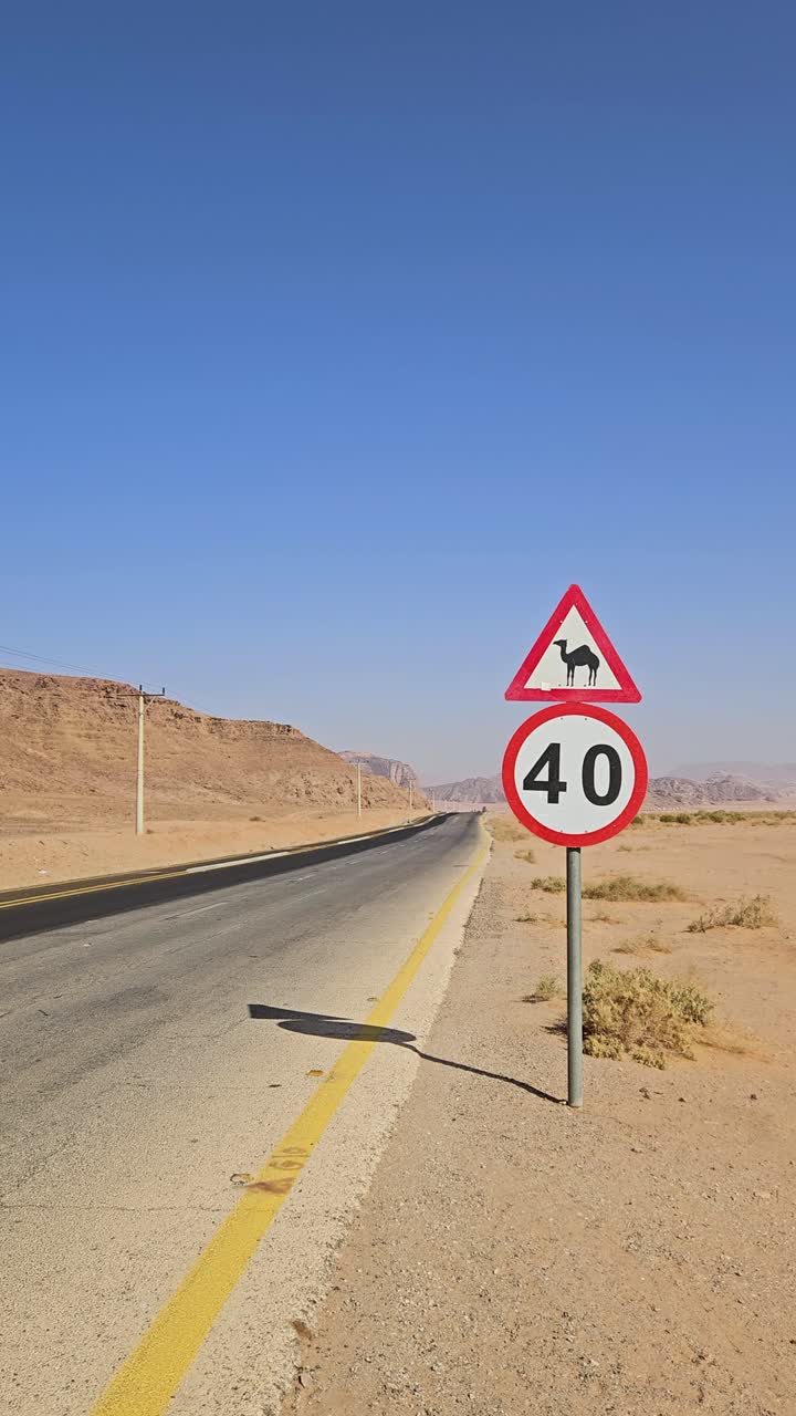 Vertical: señal de advertencia de camellos junto a una carretera de Jordania durante el día en el desierto, paneo