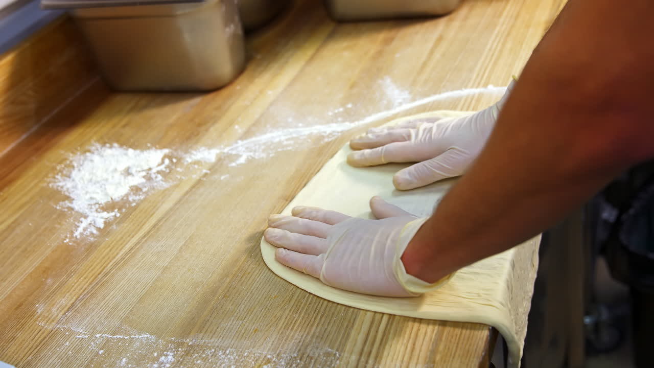 Chef forming the dough on a floured surface and kneading it with hands in a traditional pizzeria kitchen. Pizza maker prepares the dough for a tasty dish.