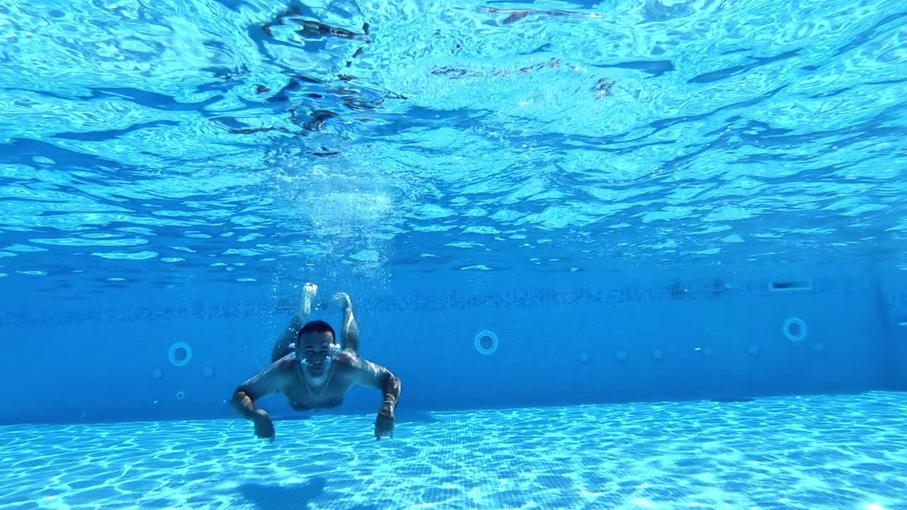 Handsome man diving into the water of the pool. Man swimming underwater in the clear water of the swimming pool. Healthy lifestyle.