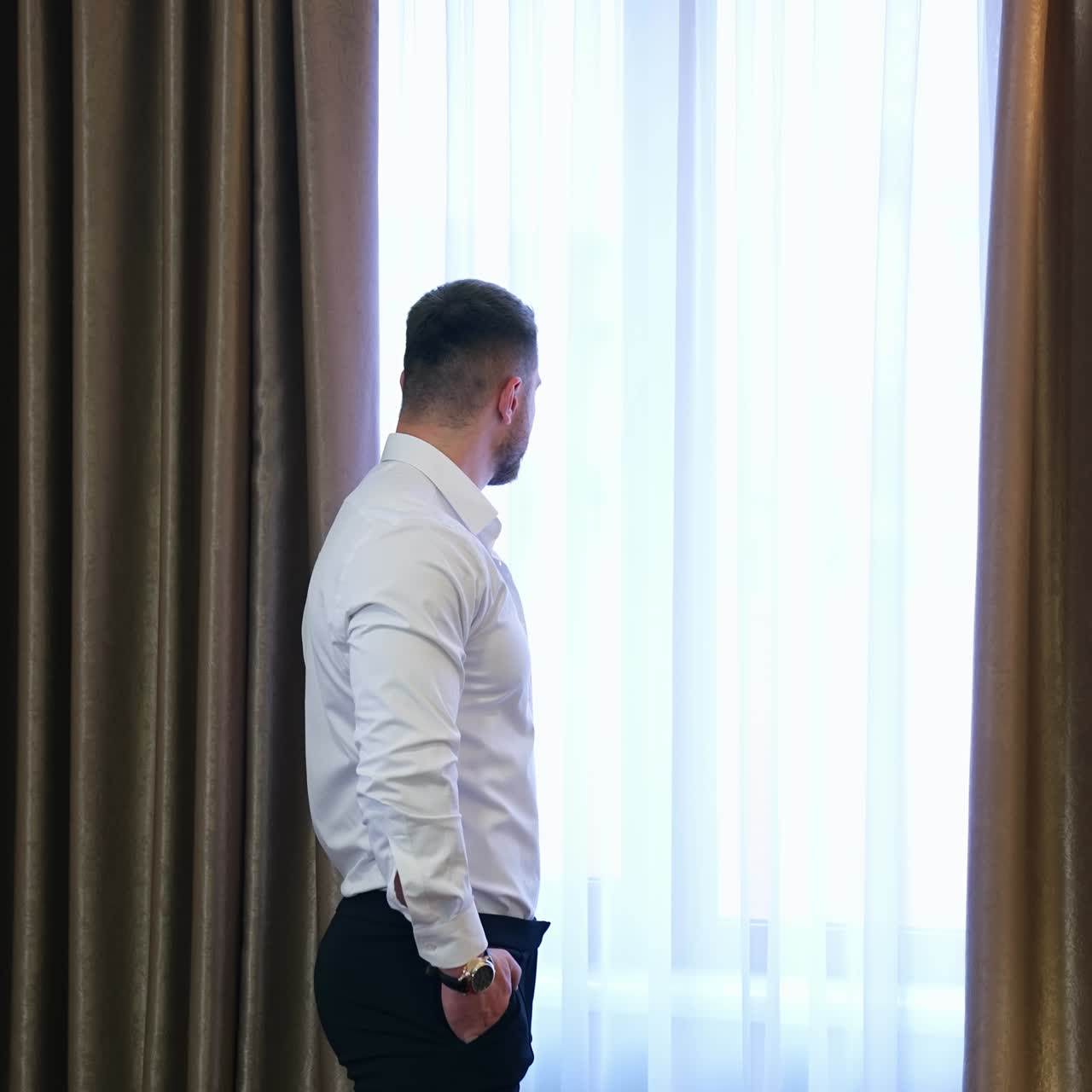 Businessman looking into the window in hotel. Man in white shirt and trousers standing near the window and dreaming. Back view