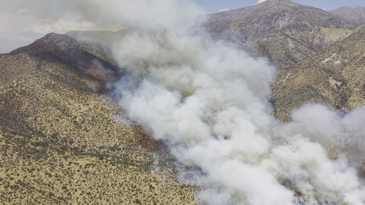 Vista aerea cinematografica ad alta quota realizzata con drone di un grande incendio che produce spessi pennacchi di fumo sul ripido versante di una montagna nelle Ande, Cile, 4K