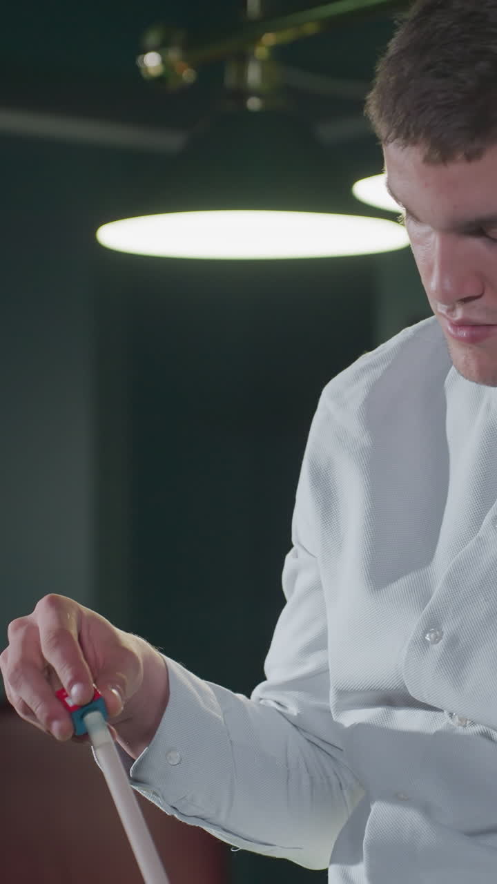 primer plano de un jugador de billar enfocado en camisa blanca aplicando cuidadosamente tiza roja al palo de la pilla. concentración intensa, configuración de sala de billar débilmente iluminada con mesa de billar verde y iluminación de fondo suave