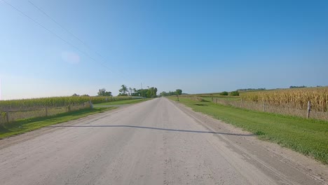 pov while driving past fields on a wide gravel road in rural iowa in late summer with wide blue sky