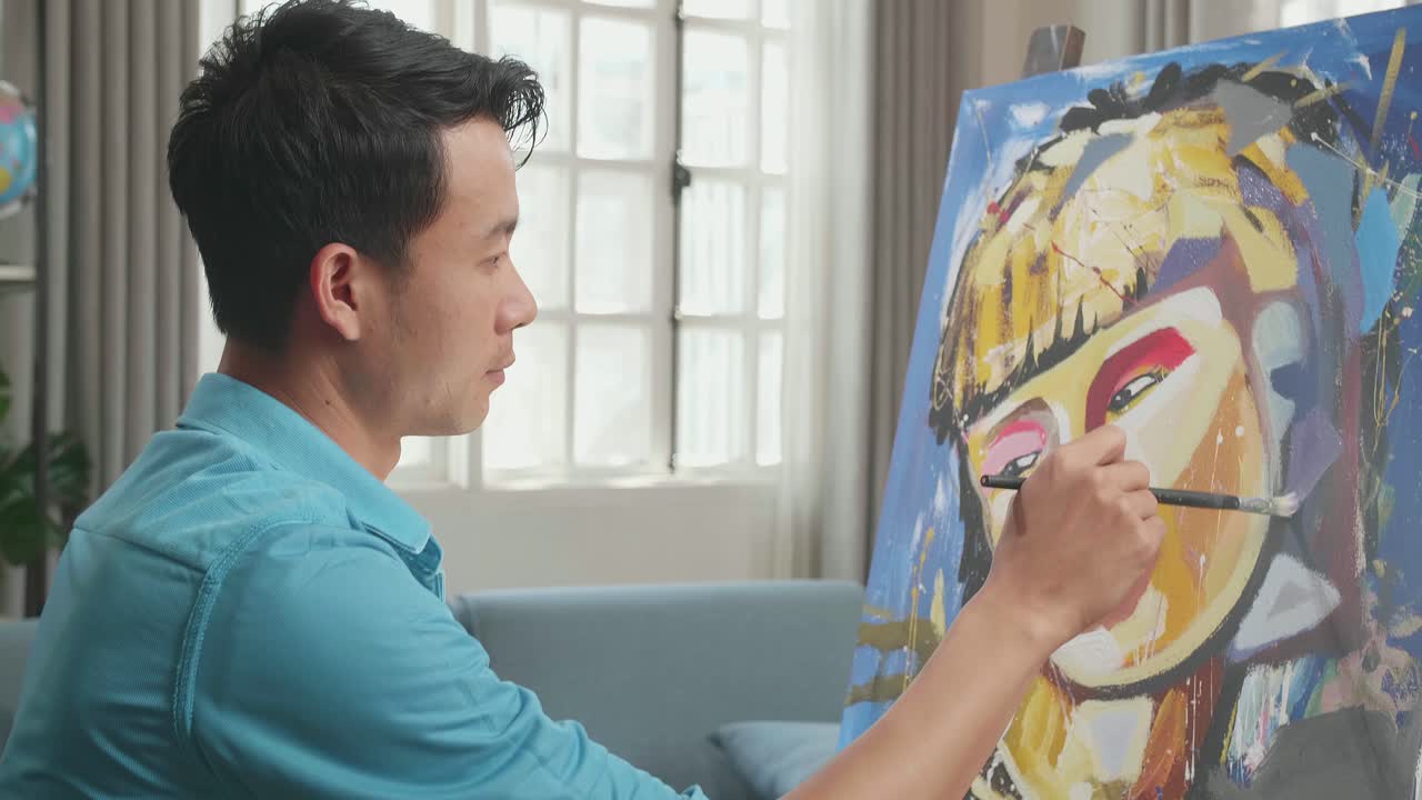 Side View Of An Asian Artist Man In Wheelchair Holding Paintbrush Mixed Colour Turn To Smile While Painting A Girl On The Canvas