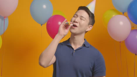 studio portrait of man wearing party hat celebrating birthday with balloons and party blower 1