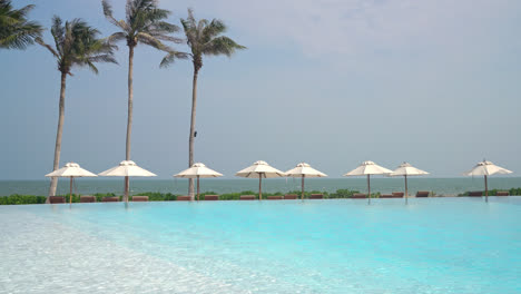 umbrella-with-bed-pool-around-swimming-pool-with-ocean-sea-background---holiday-and-vacation-concept