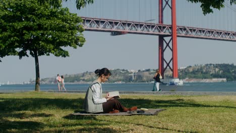 woman reading a book in a park by the bridge