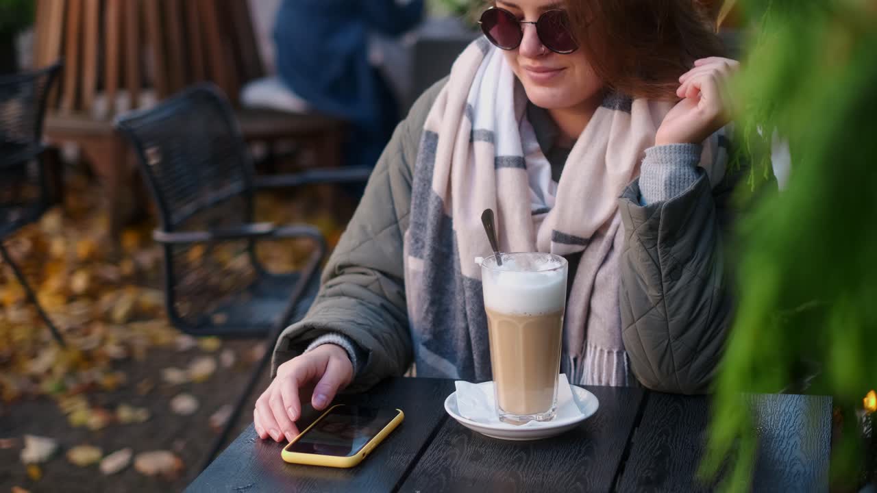 Woman using phone while having a latte in an outdoor cafe