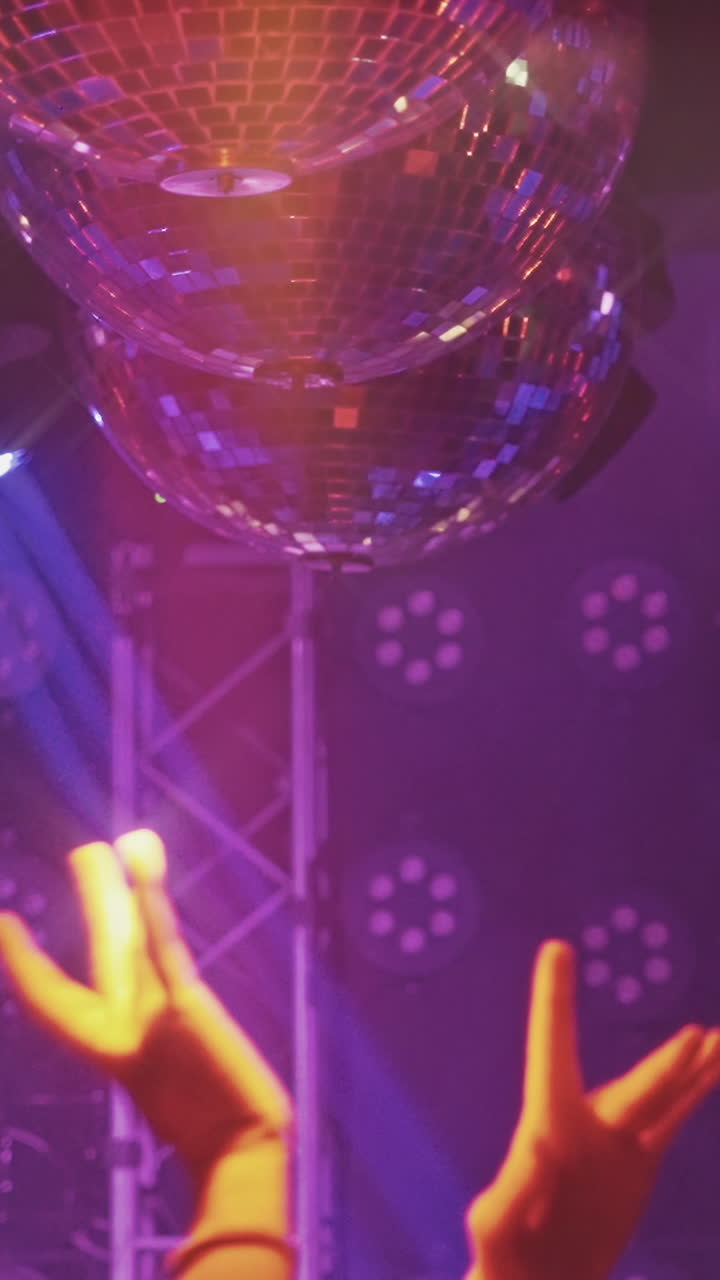 Mãos dançando sob bolas de discoteca em uma festa de boate.