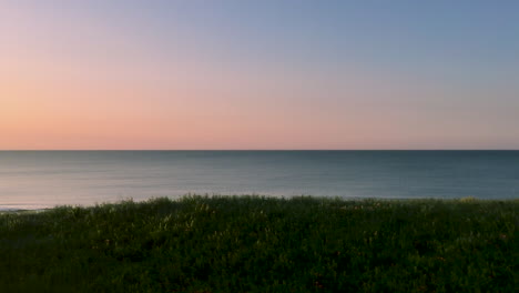 view from a slow moving train of a beautiful pastel sunset over a calm ocean with coastal green vegetation