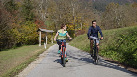 young man and girl enjoying cycle ride in nature on sunny autumn day, front view