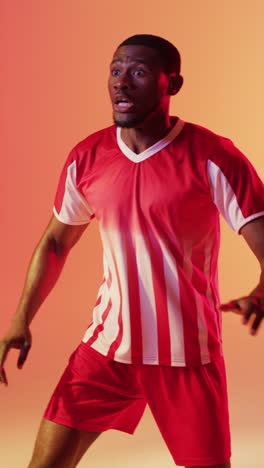 vertical video of african american male soccer player returning football over pink lighting