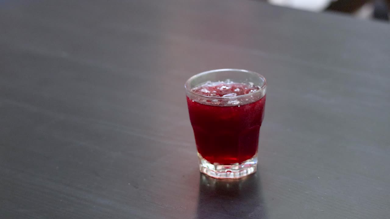 Hand placing roselle juice drinks on table in glasses