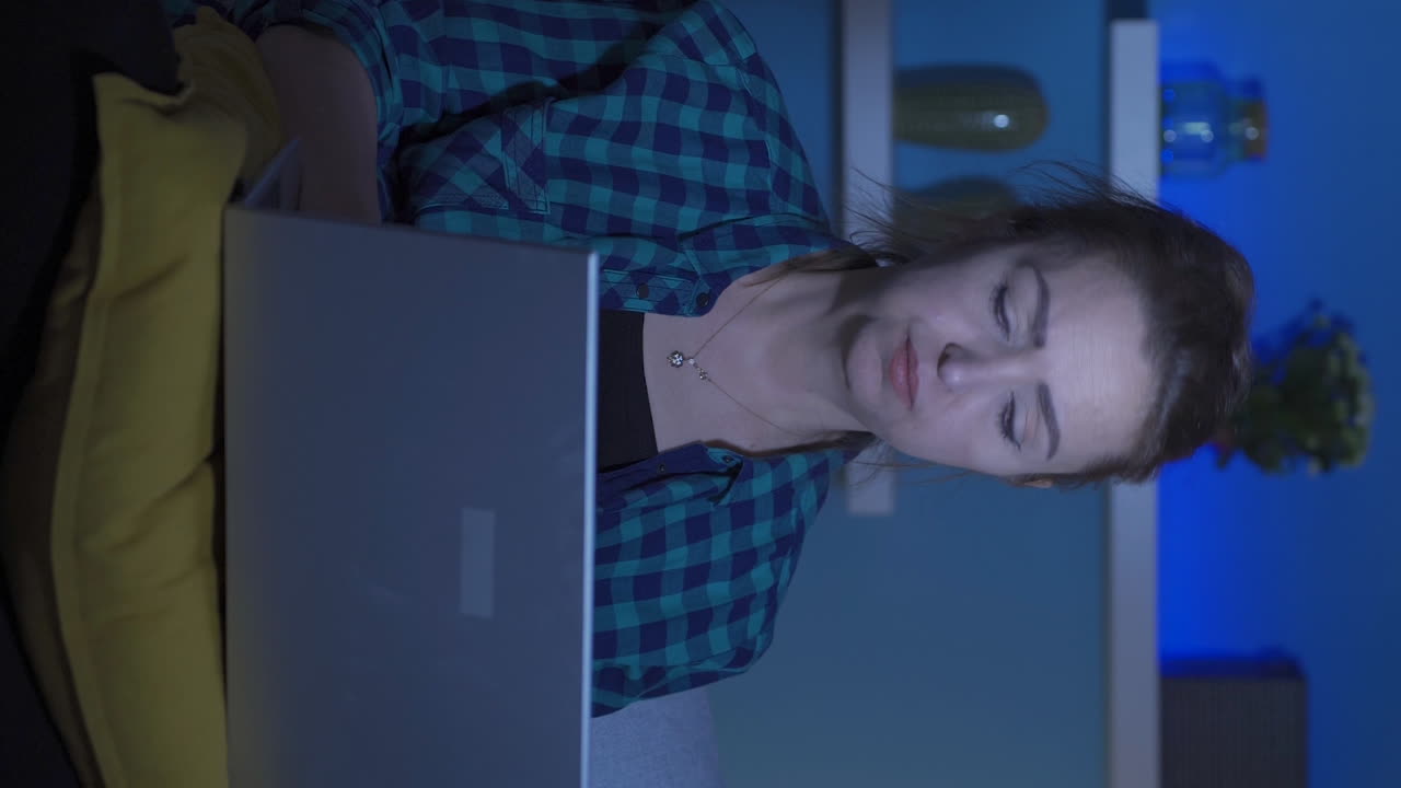 Vertical video of Unhappy woman using laptop laptop at night. It's not in a good mood.
