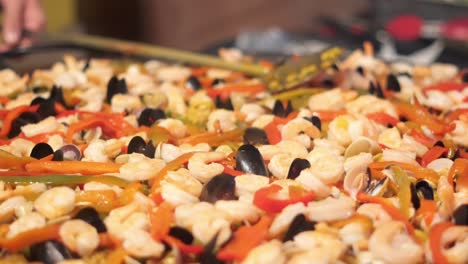 una paella enorme y caliente, hábilmente hecha, esperando a ser servida a los clientes en un restaurante, llevada con una cuchara ranura