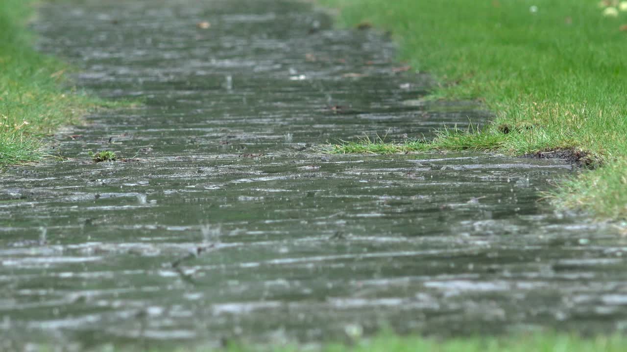 Heavy rain water drops falling on garden stone path and splashing in rainy day. 4K