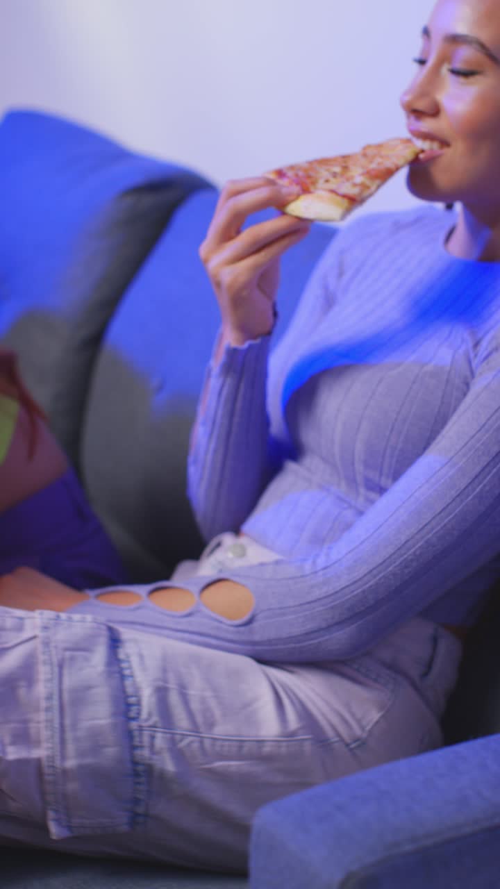 video vertical de un grupo de amigos de la generación z sentados en el sofá en casa comiendo pizza para llevar y hablando 1