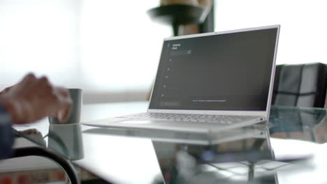 Midsection-of-african-american-man-sitting-at-desk-using-laptop-at-home,-slow-motion