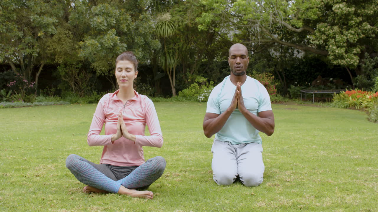 Multiracial couple meditating in peaceful garden, practicing mindfulness and relaxation together
