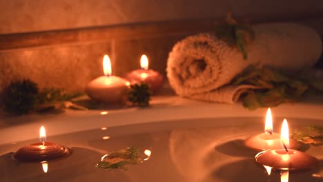 relajante fondo de spa con velas flotando en el agua del baño, algunos pétalos verdes y una toalla cerca de la superficie del agua