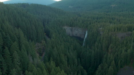 Aerial-shot-towards-a-waterfall-surrounded-by-dense-pine-forest