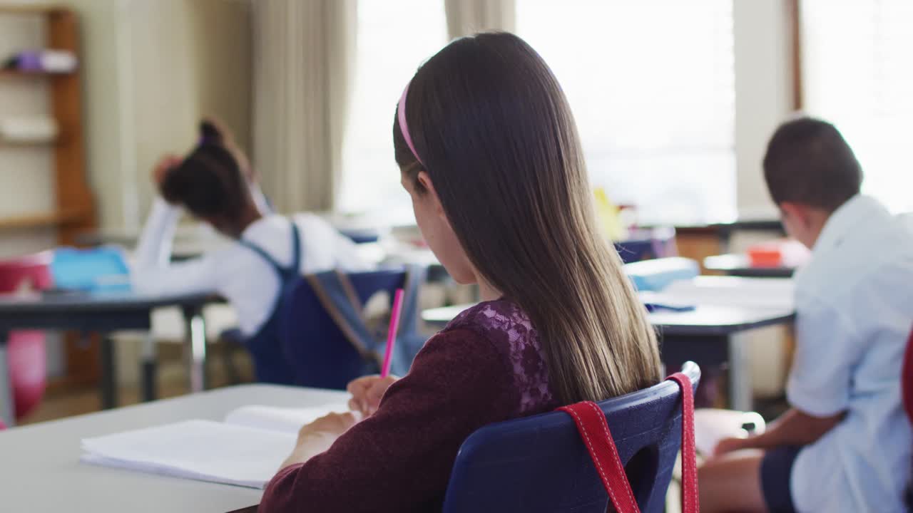 retrato de una feliz estudiante caucásica sentada en el aula, tomando notas, mirando a la cámara