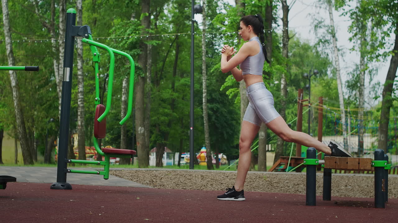 una mujer joven en un parque realiza sentadillas en una pierna en un banco en ropa deportiva en el verano. atletismo mujer caucásica entrena en el parque