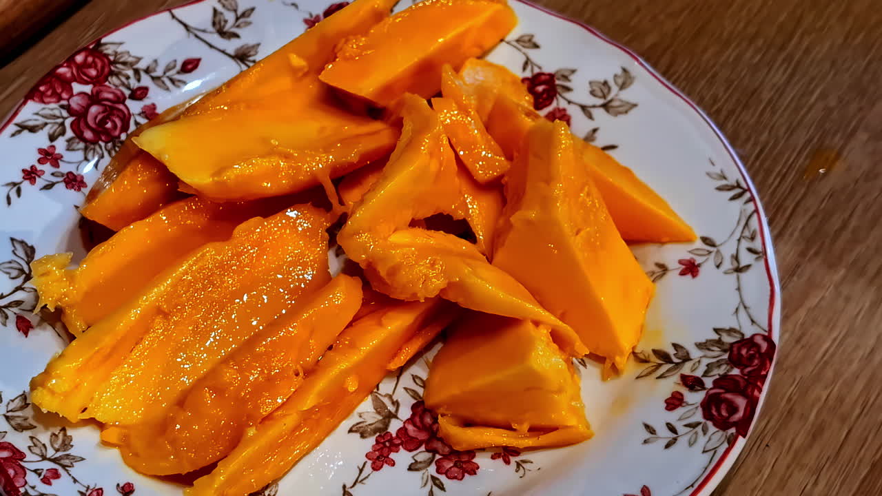 Bright orange mango slices arranged on a floral porcelain plate, ready to eat