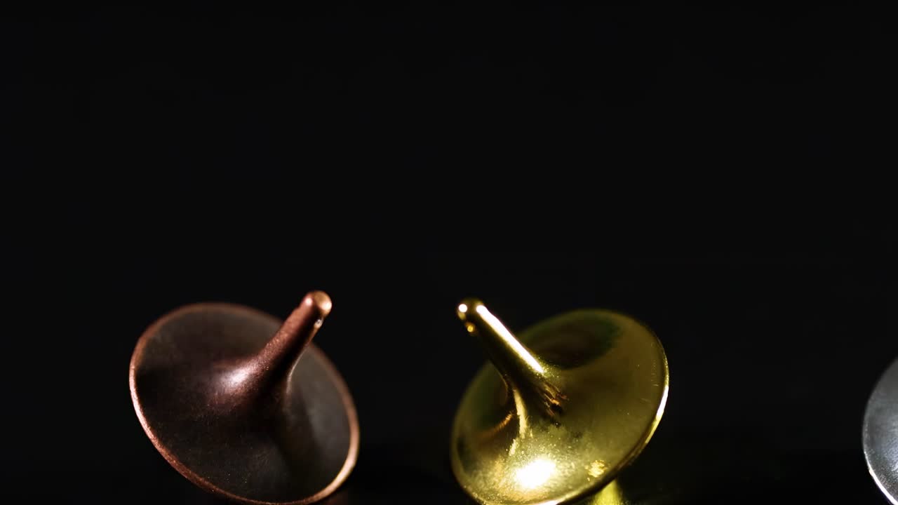 Copper, gold, and silver tops spin gracefully on a dark background, showcasing their reflective surfaces.