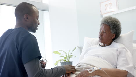 african american male doctor talking with female senior patient in hospital room, slow motion