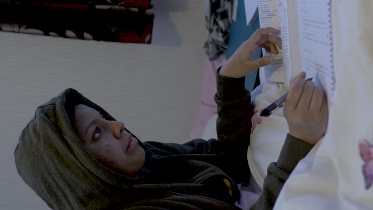 Vertical shot of Young woman doing homework at night while sitting on the bed. Tired Hispanic girl and college education. Female student studying for next day exam.