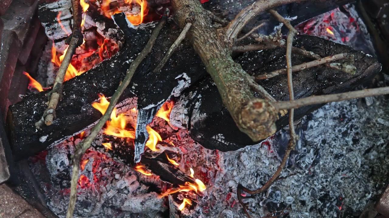 Fuoco in un focolare con legna che brucia e braci incandescenti in un campeggio di sera