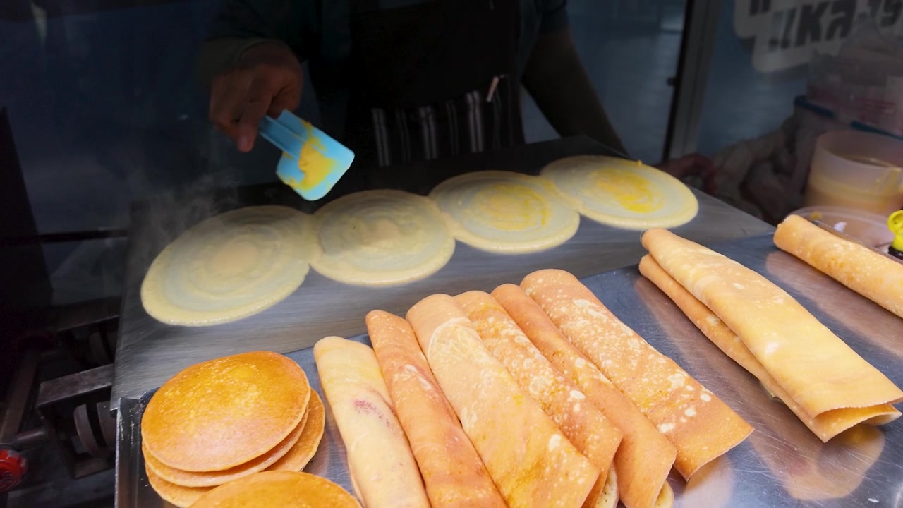 Primer plano de un vendedor extendiendo masa en una plancha de metal caliente en un mercado de Bangkok