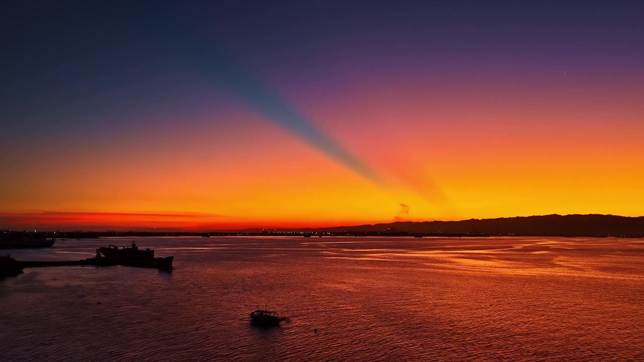 Vista aérea de un atardecer vibrante sobre mar en calma cerca del resort Dusit Thani Mactan Cebú, con barcos en el agua y nubes coloridas reflejándose en el horizonte