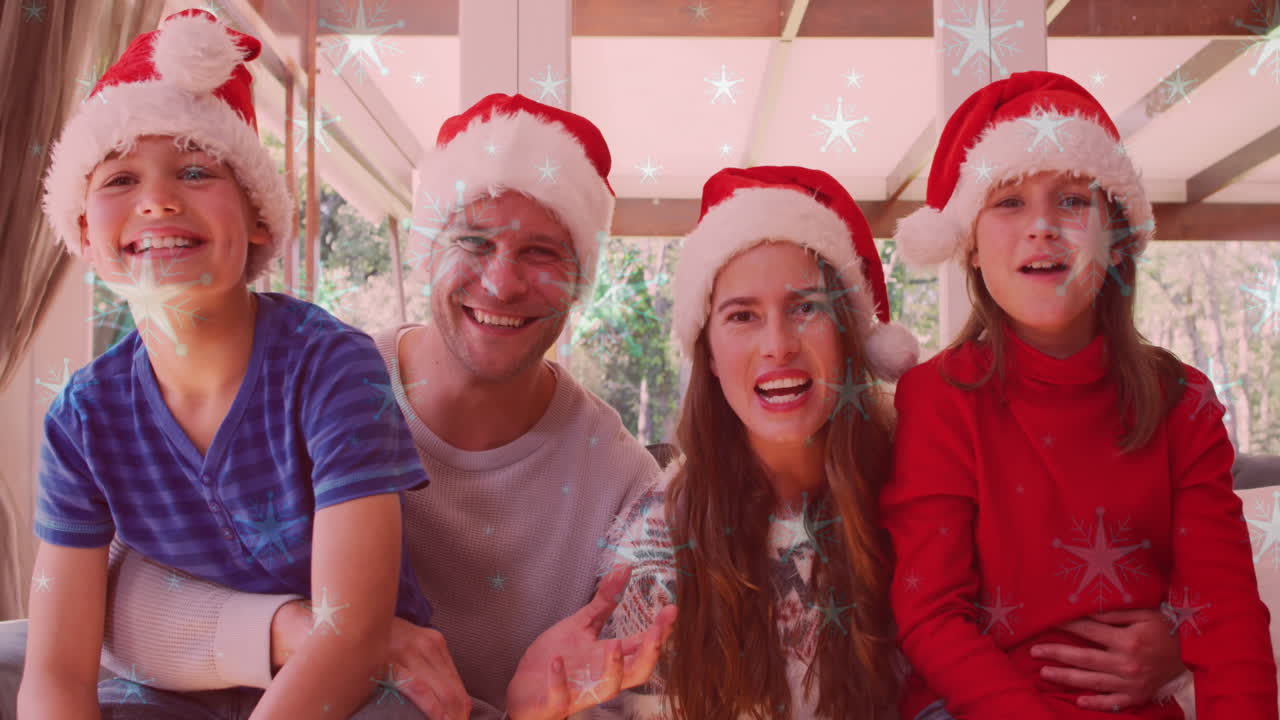 Animação de neve caindo sobre família caucasiana sorridente com gorros de Papai Noel acenando