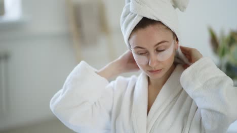 woman at home in a bathrobe and towel and patches under the eyes