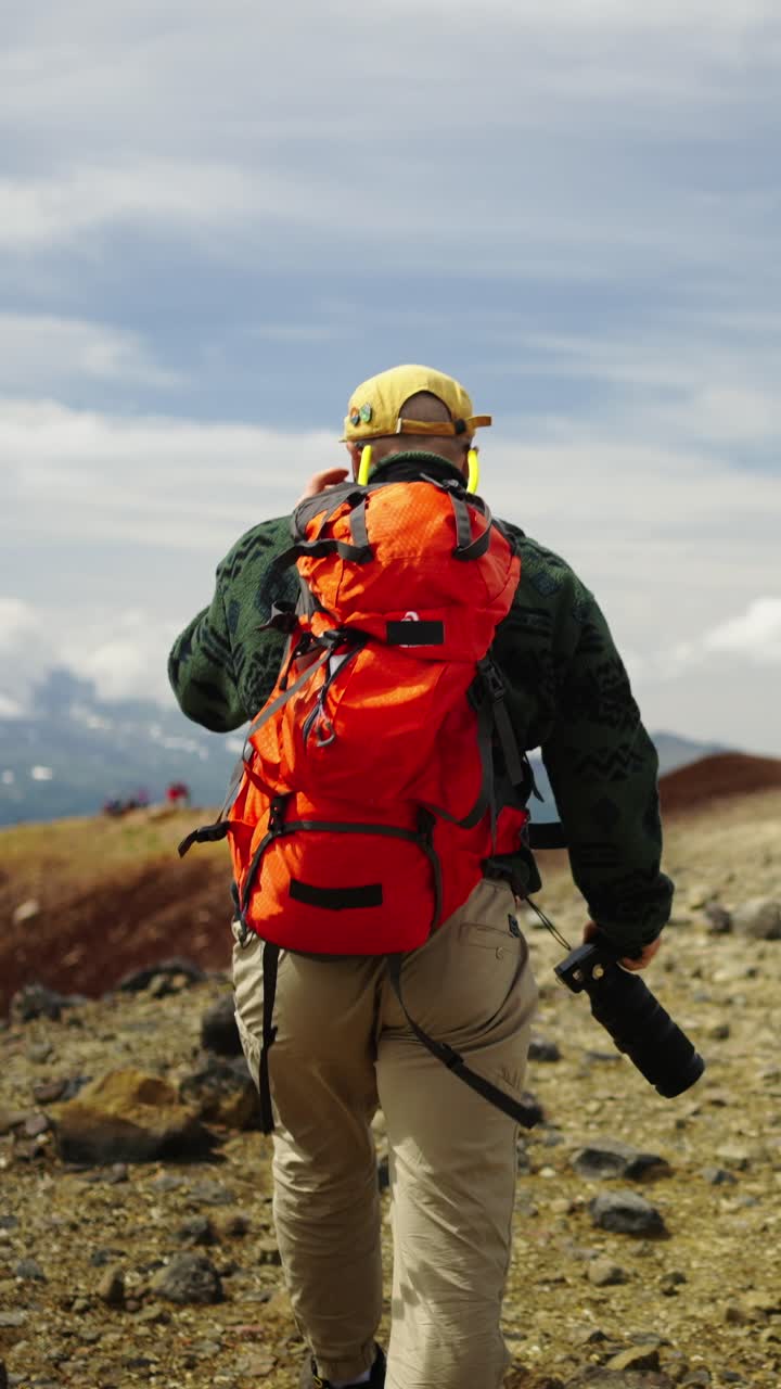 Uomo con zaino arancione e macchina fotografica che fa escursioni su una montagna rocciosa