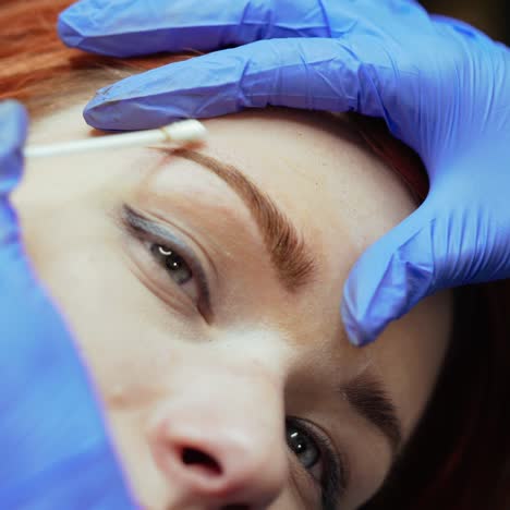 a beauty master completes the procedure of tattooing eyebrows and cleans the client's eyebrows with a cotton swab in a beauty salon. close-up
